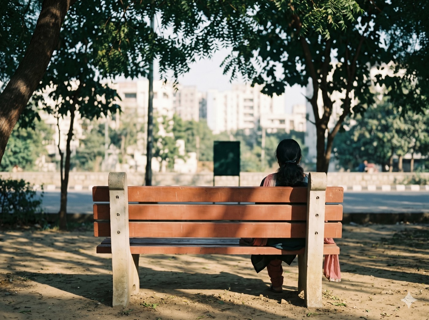 A wooden bench in dappled afternoon light, a person seen from behind, city softly visible in the background.